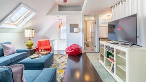 Ett modernt vardagsrum med en blå soffa, en röd fåtölj, en sittpuff, en tv och en bokhylla.