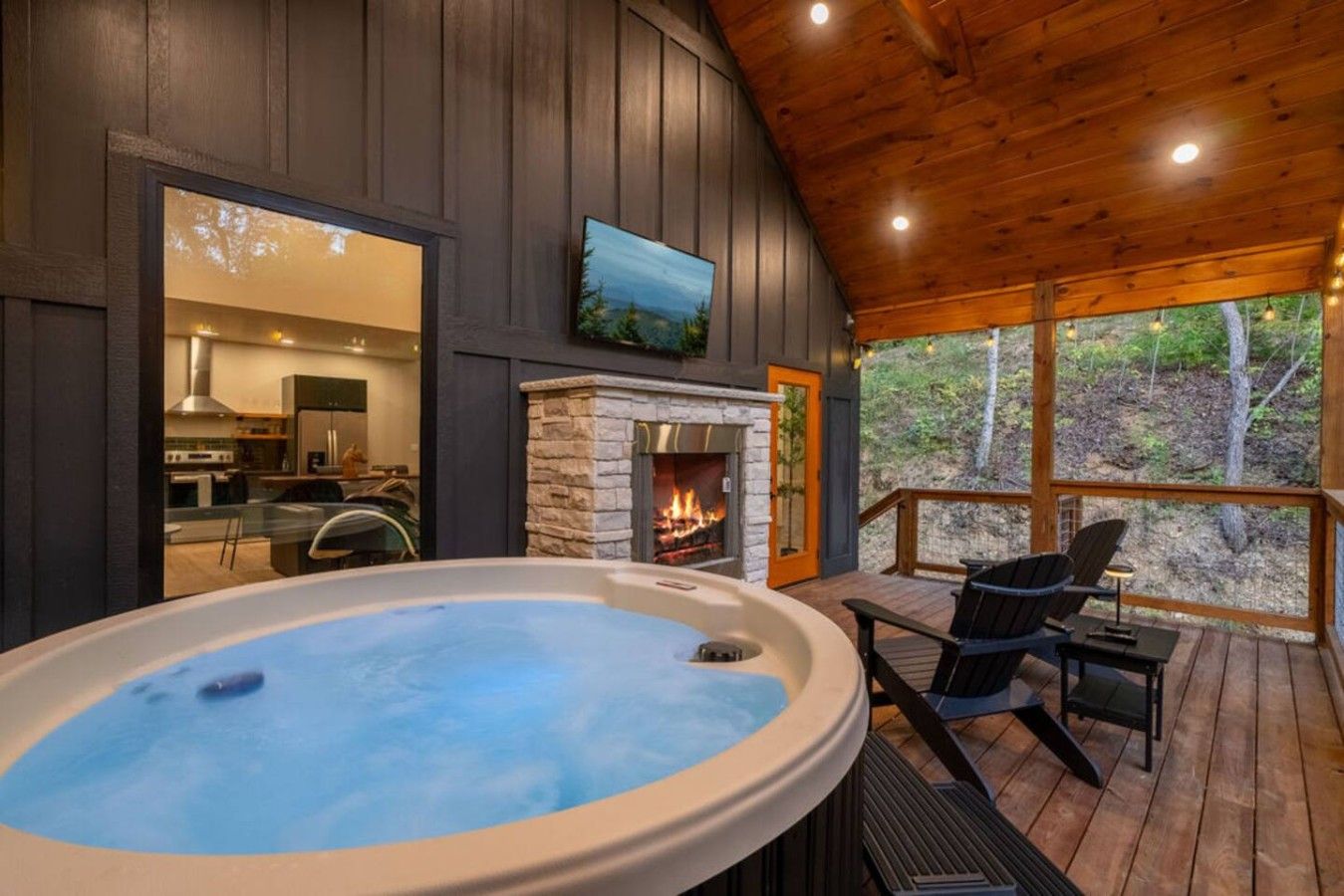 A hot tub on a wooden deck with a fireplace and a view of the outdoors.
