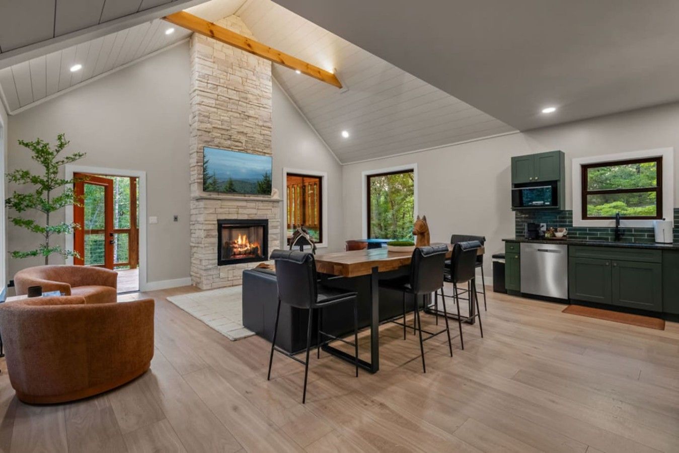A modern kitchen with a stone fireplace, dining area, and green cabinets.