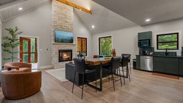 A modern kitchen with a stone fireplace, dining area, and green cabinets.
