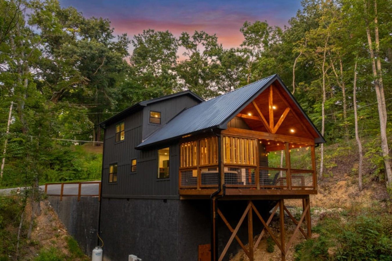 A cabin with a wooden deck and a metal roof, surrounded by trees.