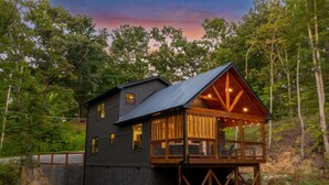Una baita con veranda in legno e tetto in metallo, immersa tra gli alberi.