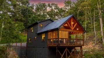 A cabin with a wooden deck and a metal roof, surrounded by trees.