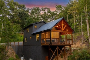 A cabin with a wooden deck and a metal roof, surrounded by trees. - Blackstone Hot Tub • Game Loft (Sevierville)