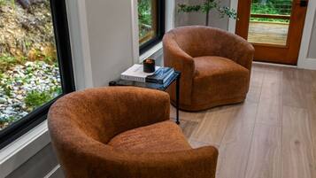 A room with two brown armchairs, a small table with a book and a cup, and a view of a garden through a window.