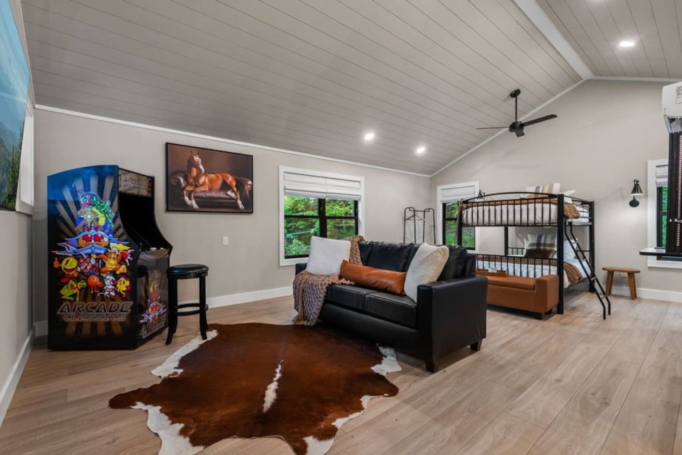 A living room with a black sofa, a brown leather rug, a gaming console, and a bunk bed.