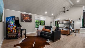 A living room with a black sofa, a brown leather rug, a gaming console, and a bunk bed.