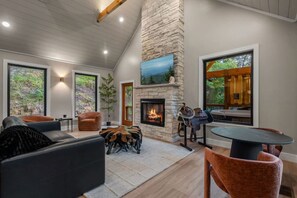 A spacious living area with a stone fireplace, comfortable seating, and large windows offering views of the outdoors.