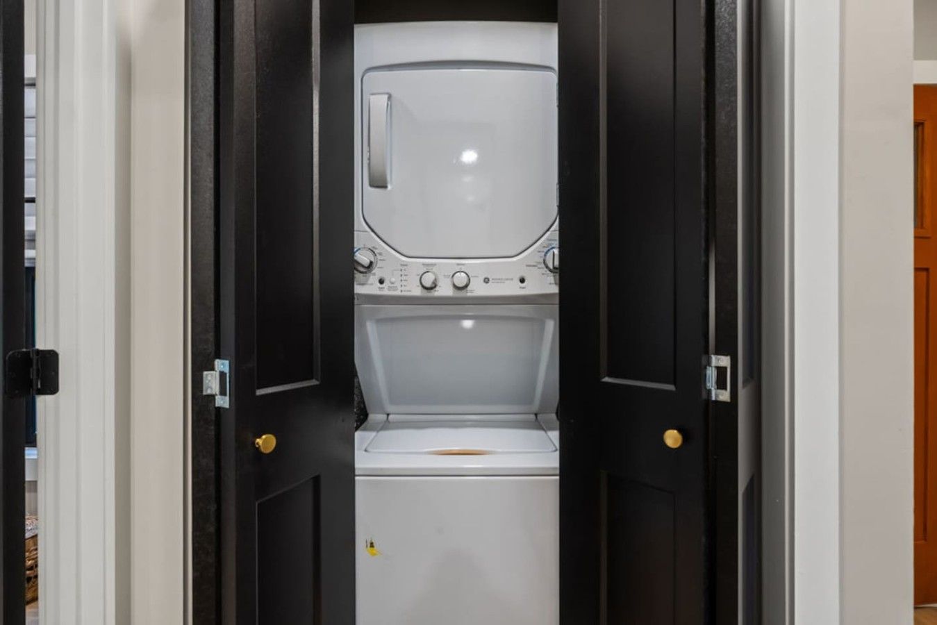Une buanderie équipée d’un lave-linge et d’un sèche-linge, une porte avec une poignée dorée et un mur blanc.