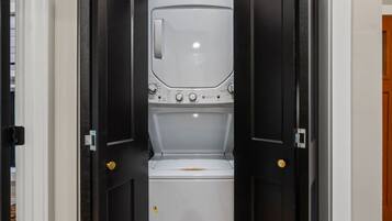 Une buanderie équipée d’un lave-linge et d’un sèche-linge, une porte avec une poignée dorée et un mur blanc.