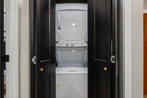 A laundry room with a washing machine and dryer, a door with a golden handle, and a white wall. - Blackstone Hot Tub • Game Loft (Sevierville)