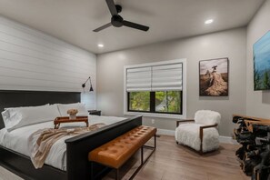 A bedroom with a bed, a bench, a chair, a ceiling fan, and a window with blinds. - Blackstone Hot Tub • Game Loft (Sevierville)