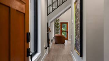 Un couloir avec un escalier, une porte, une chaise et une porte dotée d’un panneau en verre.