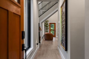 A hallway with a staircase, a door, a chair, and a door with a glass panel. - Blackstone Hot Tub • Game Loft (Sevierville)