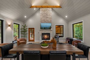 A spacious dining area with a large wooden table, leather chairs, a stone fireplace, and large windows offering views of the outdoors. - Blackstone Hot Tub • Game Loft (Sevierville)
