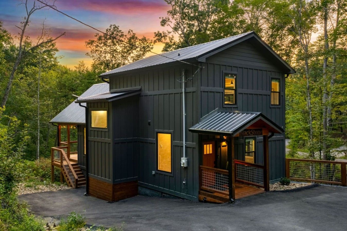 A two-story cabin with a porch and a covered entryway, surrounded by trees.