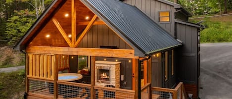 A wooden cabin with a fireplace, a hot tub, and a deck.