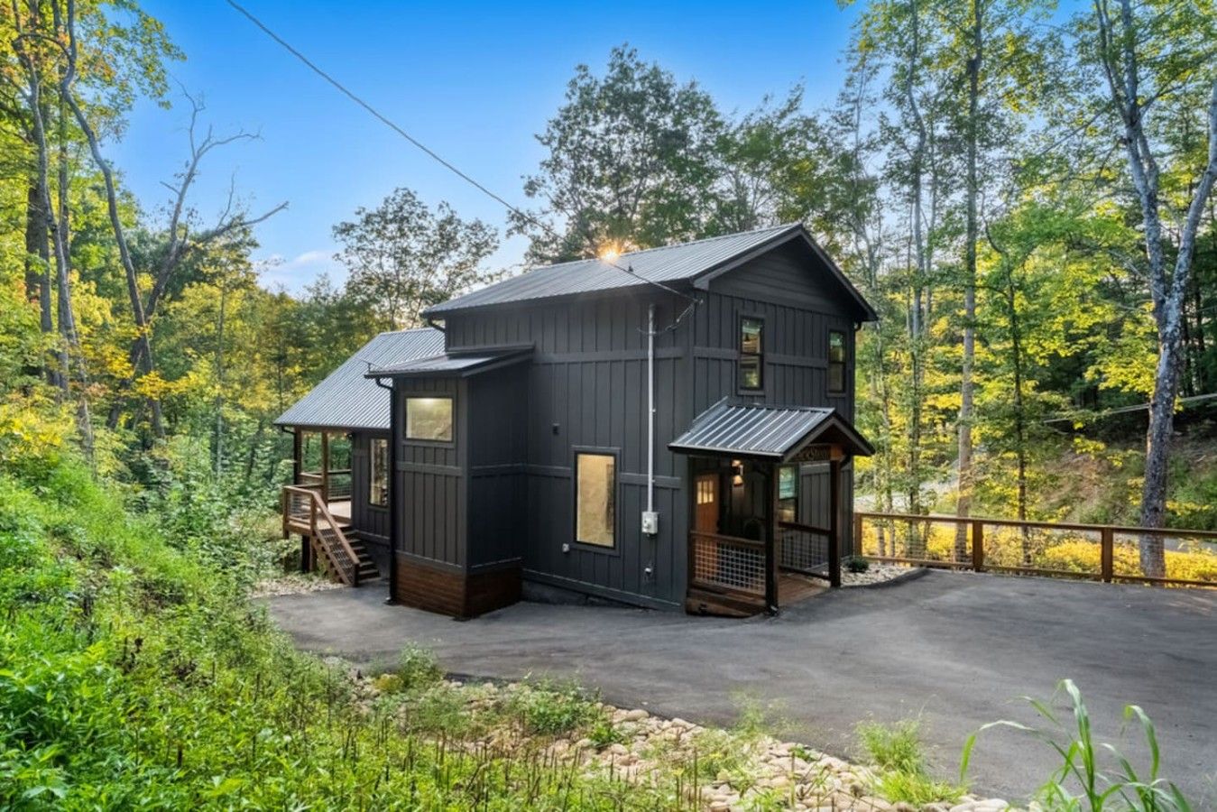 Une cabane à deux étages dotée d’un porche couvert et d’une petite terrasse, entourée d’une forêt dense.