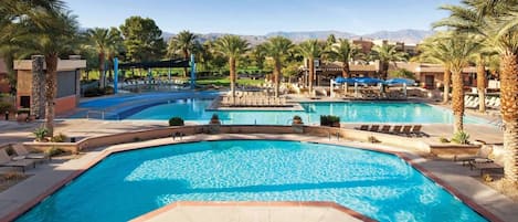 A large outdoor swimming pool with multiple sections, surrounded by palm trees and lounge chairs.