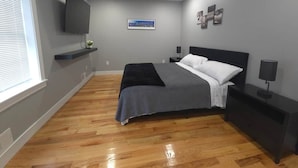 A bedroom with a bed, a TV mounted on the wall, a window with blinds, and a picture on the wall. - Apartment in Newark,
sleeps 5+, spacious & near NY (Newark)