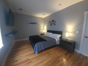 A bedroom with a bed, bedside tables, a wall-mounted TV, and a window.