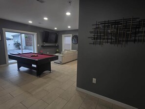 A room with a pool table, a sofa, and a television.