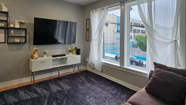 A living room with a flat-screen TV, a white console table, a dark carpet, a window with white curtains, and a brown sofa. - Apartment in Newark,
sleeps 5+, spacious & near NY (Newark)