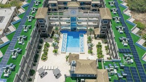 A hotel with a central swimming pool, multiple balconies, and solar panels. - New Ground Floor 1BR Condo ~ Close to Eagle Beach (Noord)