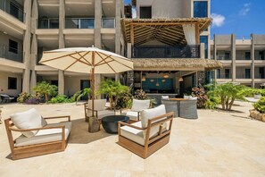 A hotel courtyard with outdoor seating, a thatched-roof structure, and a pool area. - New Ground Floor 1BR Condo ~ Close to Eagle Beach (Noord)