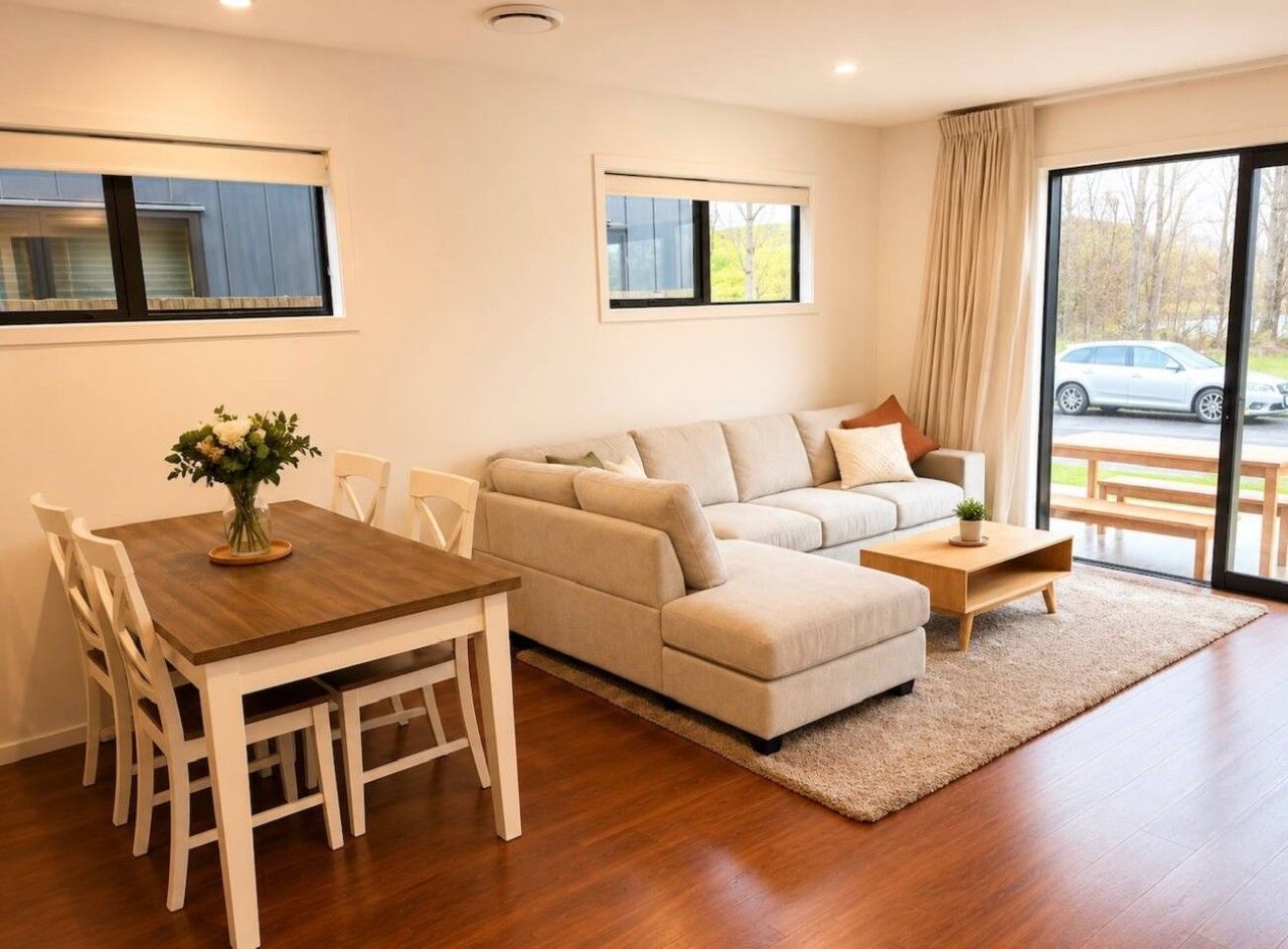 Una sala de estar moderna con sofá, mesa de centro, mesa de comedor, sillas y vista a través de un ventanal.