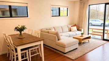 Una sala de estar moderna con sofá, mesa de centro, mesa de comedor, sillas y vista a través de un ventanal.