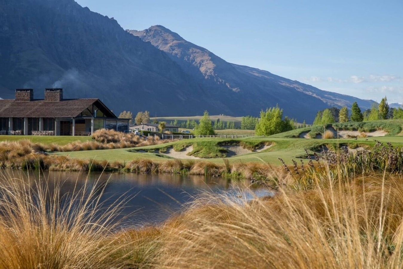 Un campo de golf con un club de campo, un estanque y montañas al fondo.