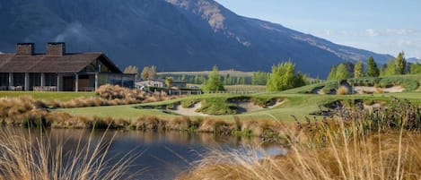 Un campo de golf con un club de campo, un estanque y montañas al fondo.