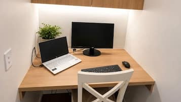 Un espacio de trabajo pequeño y ordenado con una computadora portátil, dos monitores, un teclado, un ratón y una silla.