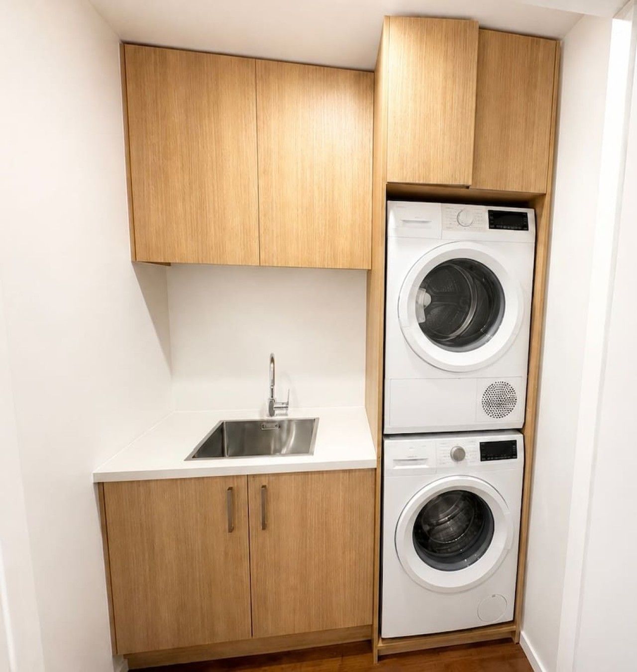 A compact laundry area with a sink and two stacked washing machines.