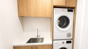 A compact laundry area with a sink and two stacked washing machines.