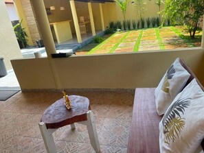 A room with a wooden table and a cushioned bench, a small potted plant, and a view of a garden with a patterned lawn and trees.