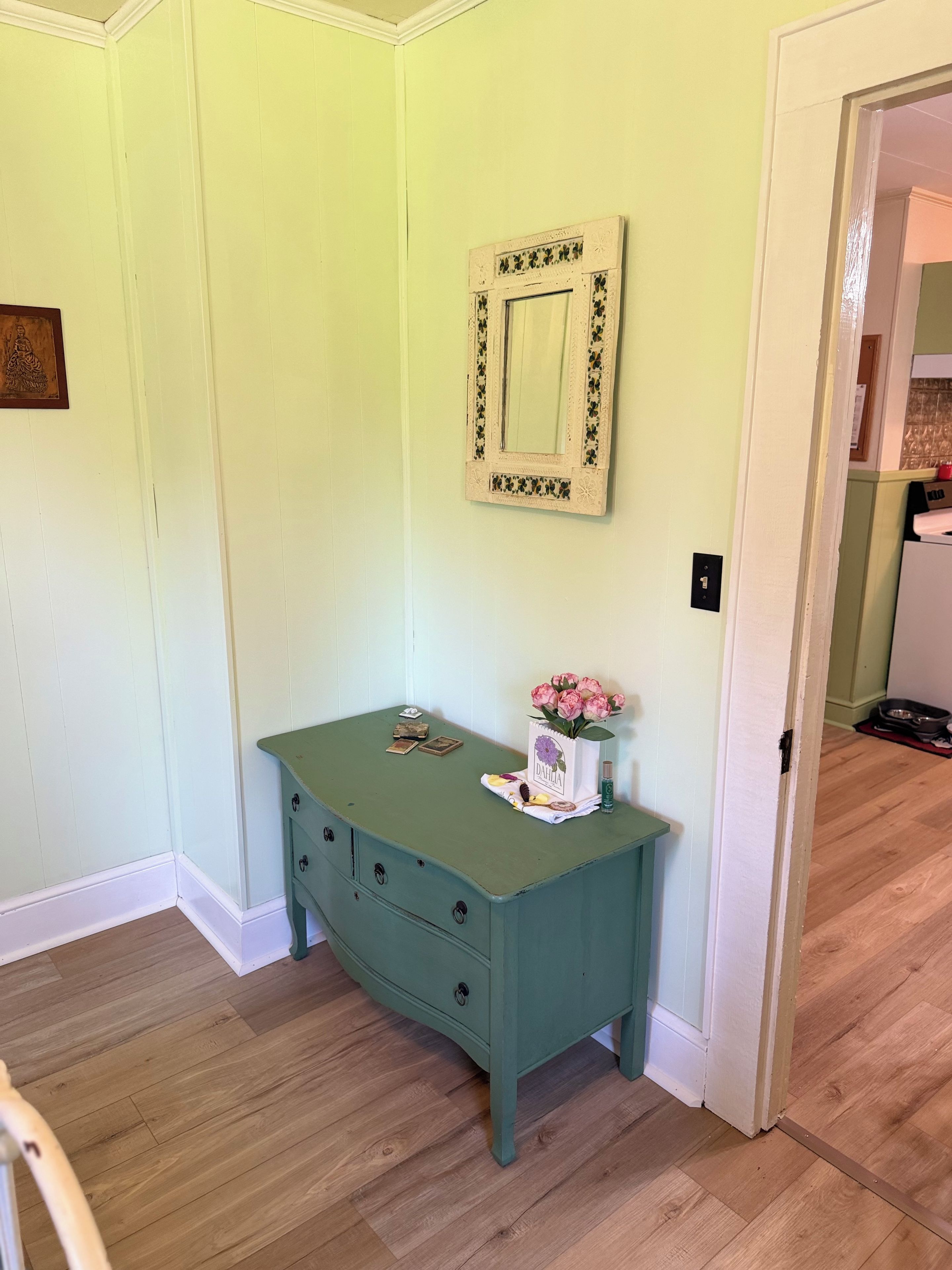 A teal dresser with drawers, a mirror, and a vase with flowers.