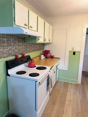 A kitchen with a white stove, green cabinets, and a patterned backsplash.