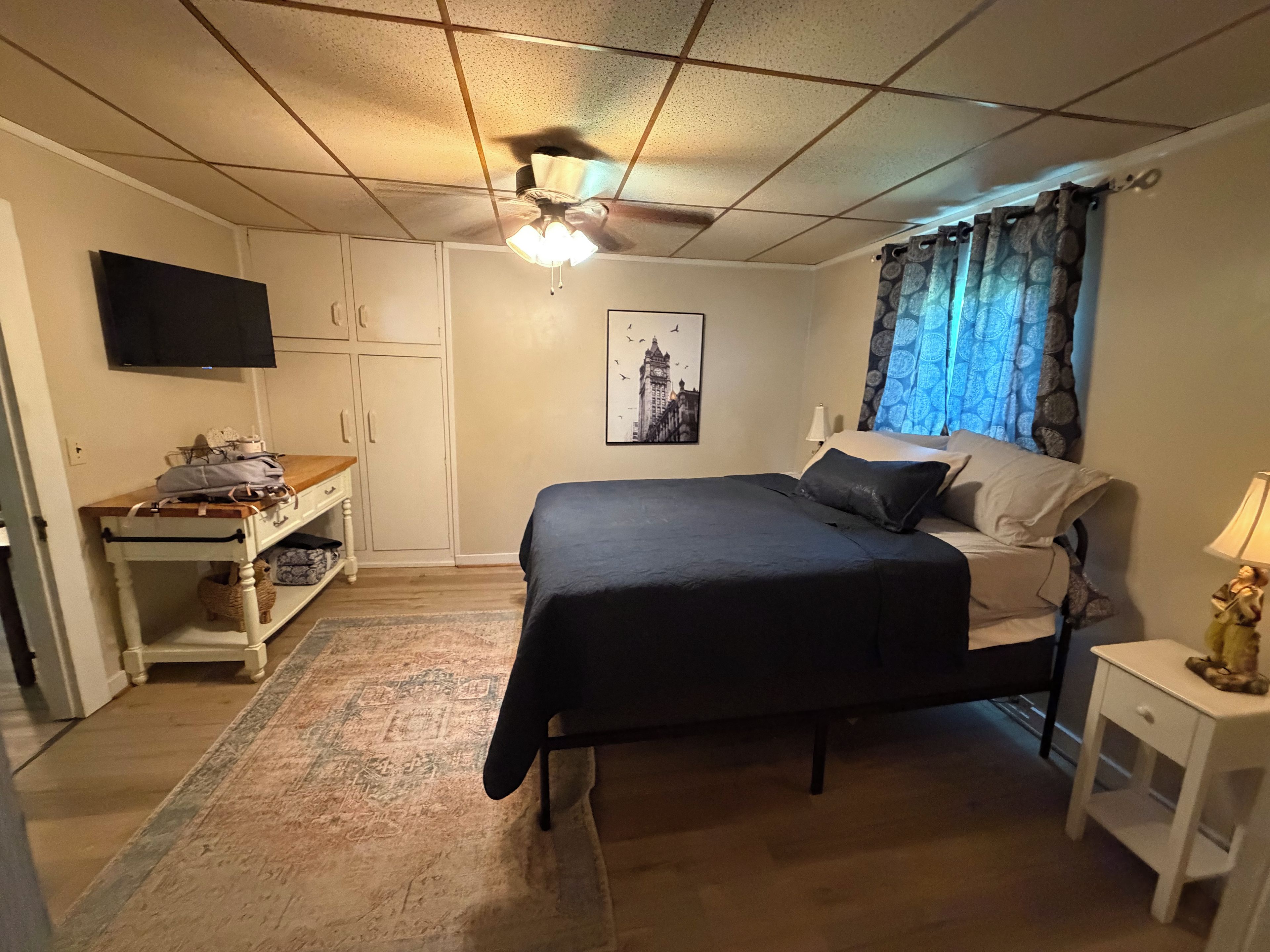 A bedroom with a bed, a desk, a television, and a window with curtains.