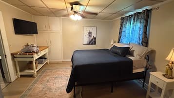 Une chambre à coucher avec un lit, un bureau, une télévision et une fenêtre avec des rideaux.