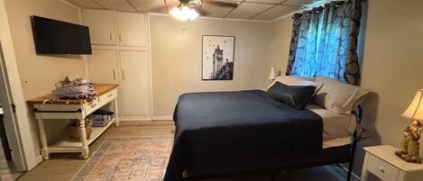 A bedroom with a bed, a desk, a television, and a window with curtains.