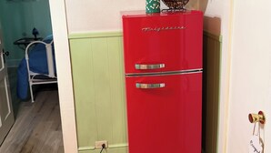 Un frigorifero rosso con un biglietto sulla porta, un quadro appeso al muro e una sedia blu sullo sfondo.