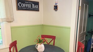 Un'area ristorazione con un tavolo rotondo e sedie rosse, un cartello per la caffetteria al muro e una finestra con tende.
