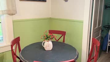 Un coin repas avec une table ronde et des chaises rouges, un panneau indiquant un bar à café sur le mur, et une fenêtre avec des rideaux.