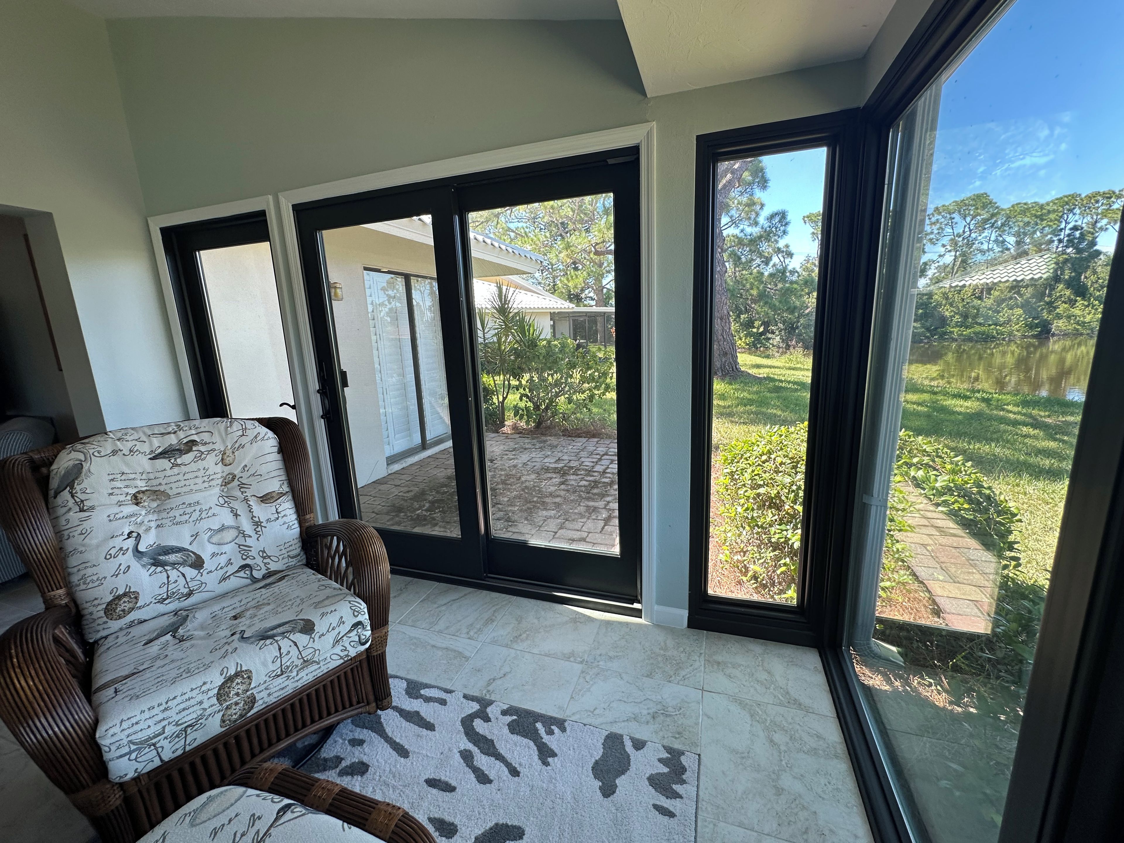 A room with a wicker sofa and a view of a garden through large glass doors.