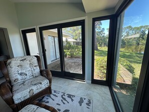 A room with a wicker sofa and a view of a garden through large glass doors. - Serene 2 Bedroom 2 Bath Villa with Lakeview in Myrtle Trace (Venice)