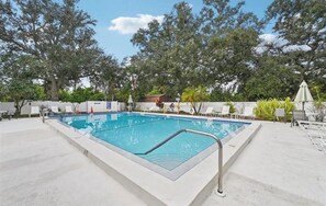 A rectangular swimming pool with a metal ladder, surrounded by white lounge chairs and umbrellas, with trees in the background. - Serene 2 Bedroom 2 Bath Villa with Lakeview in Myrtle Trace (Venice)