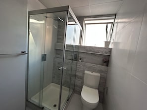 A modern bathroom with a glass-enclosed shower, a toilet, and a window providing natural light. - Cala Cala Apartment (Cochabamba)