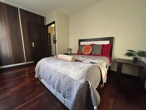 Ein Schlafzimmer mit einem Bett, einem Nachttisch, einer Topfpflanze und einem Holzschrank.